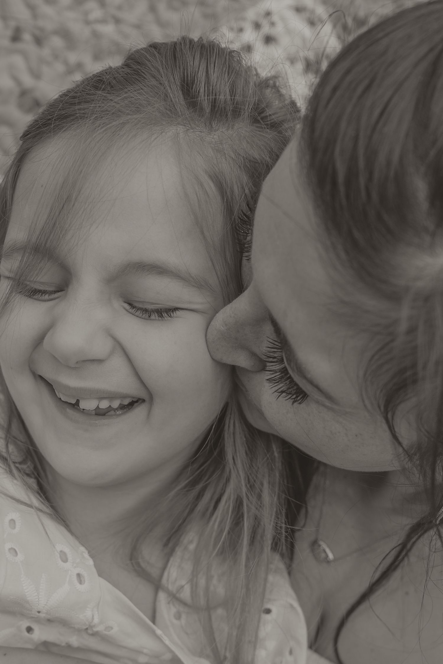Black and white photo of a mother cuddling two young daughters on a patchwork quilt blanket outdoors.