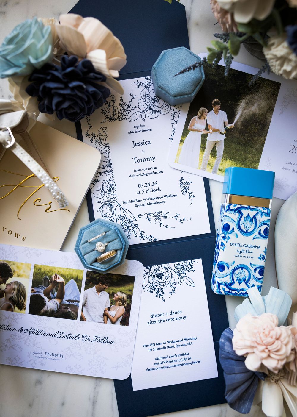 Wedding stationery flat lay featuring navy blue invitations, engagement photos, rings, and floral accents for Jessica and Tommy.