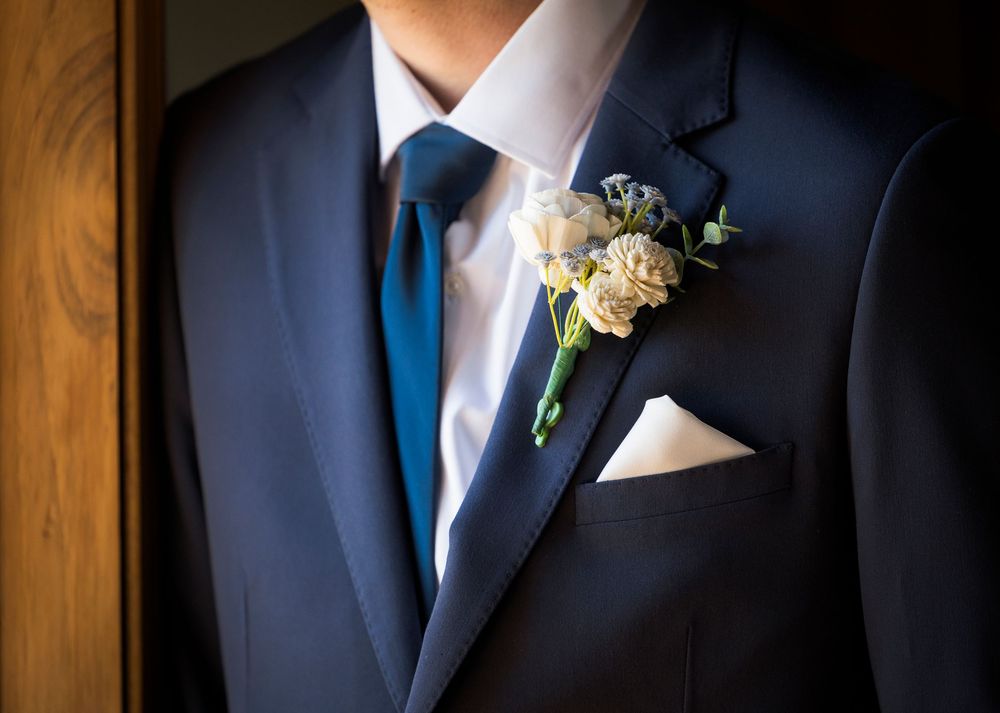 Groom in navy suit with floral boutonniere and white pocket square on wedding day.