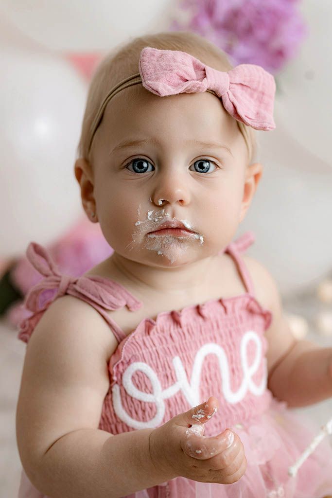 Close-up of baby girl with cake on her face wearing a pink 'one' dress during her first birthday smash.