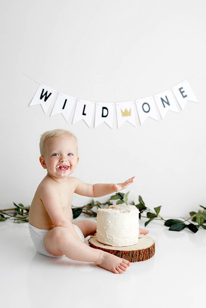 Baby boy smash cake photo session with Wild One banner and white frosted cake on wood slice by Riverside cake smash photographer.