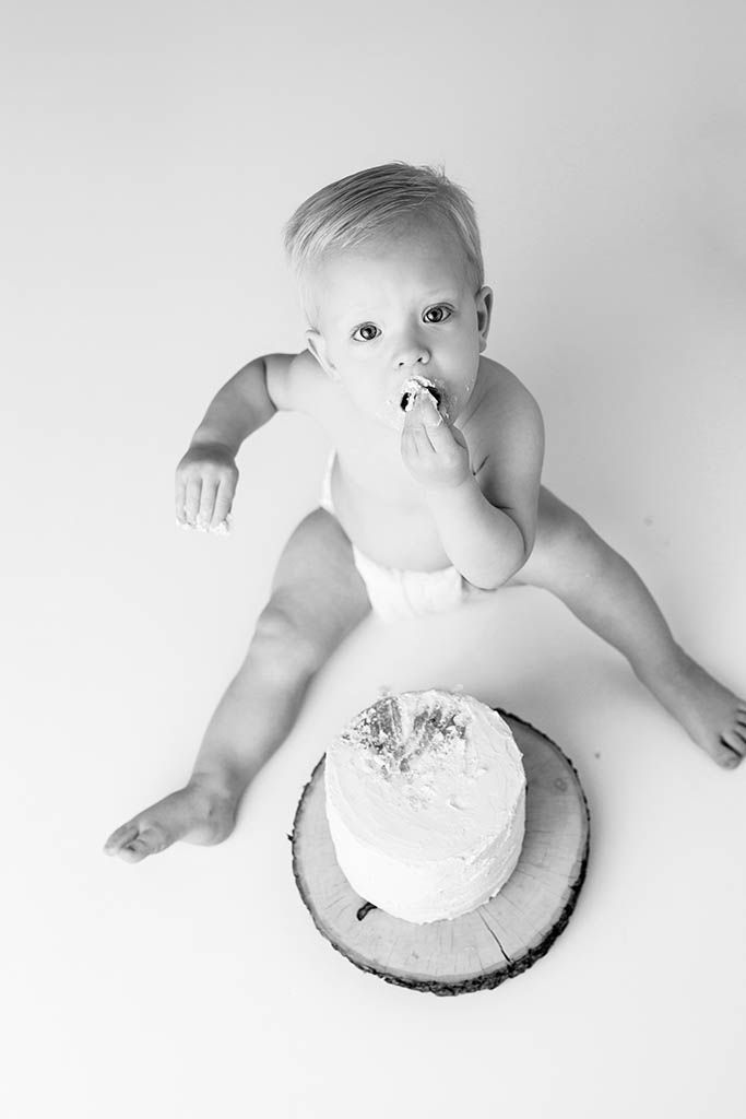 Black and white photo of a baby in a diaper eating cake during a first birthday smash cake session by Riverside cake smash photographer.