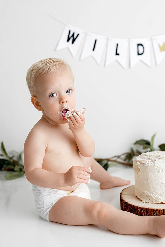 Baby in diaper eating cake at a Wild-themed first birthday cake smash photoshoot with white background.