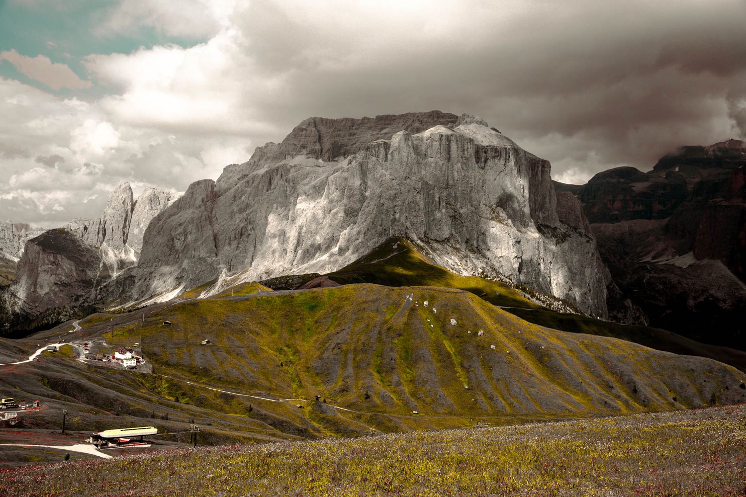 Dramatic Dolomite mountains with jagged rocky peaks, winding road, and moody overcast sky in the Italian Alps.