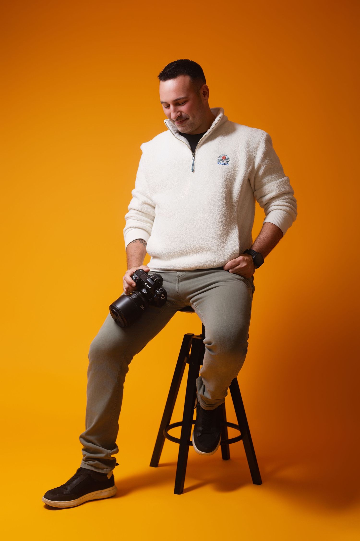 Person in cream sweater and light pants sits on dark wooden stool against vibrant orange background in various poses.