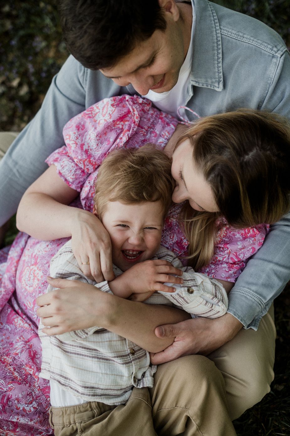 A joyful family moment with parents hugging and laughing with their young toddler son outdoors.