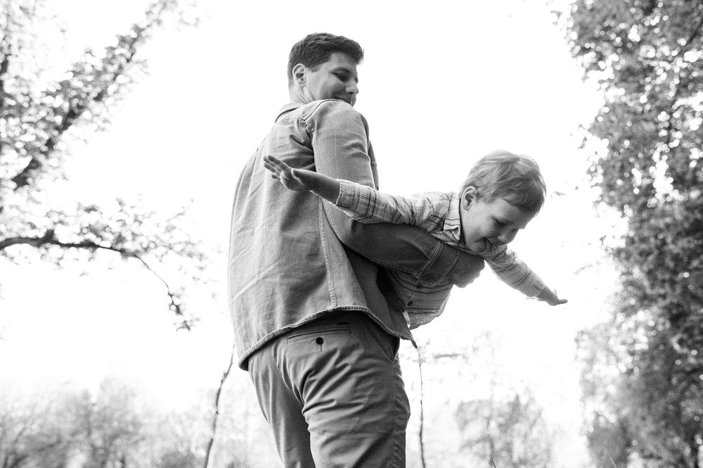 Father playfully lifting his young son outdoors in a black and white photo.