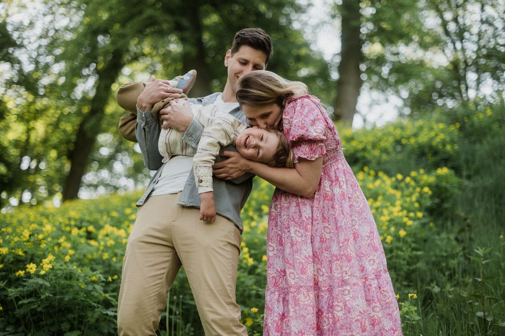 A joyful family of three plays together in a lush green field with yellow wildflowers.