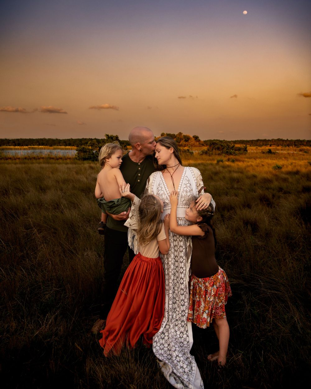 Family of four sharing a tender moment in a field during sunset.