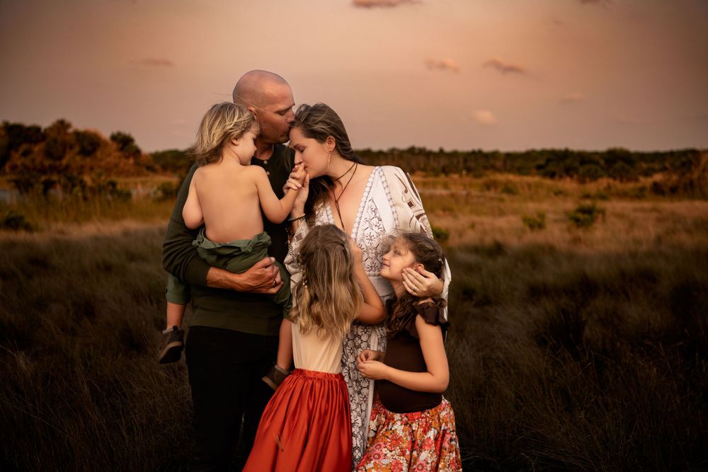 Family embracing together in an open field during a warm sunset.