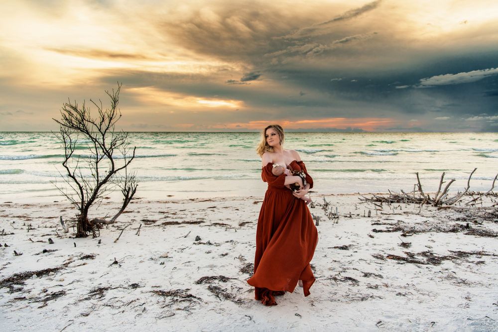 Woman in red dress walking on snowy beach at dramatic sunset.