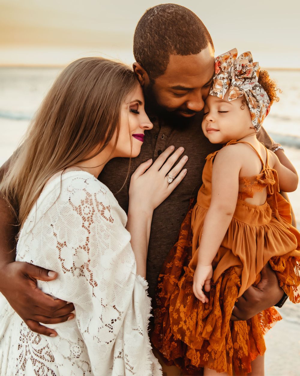Interracial family sharing a loving moment on the beach with their baby girl.