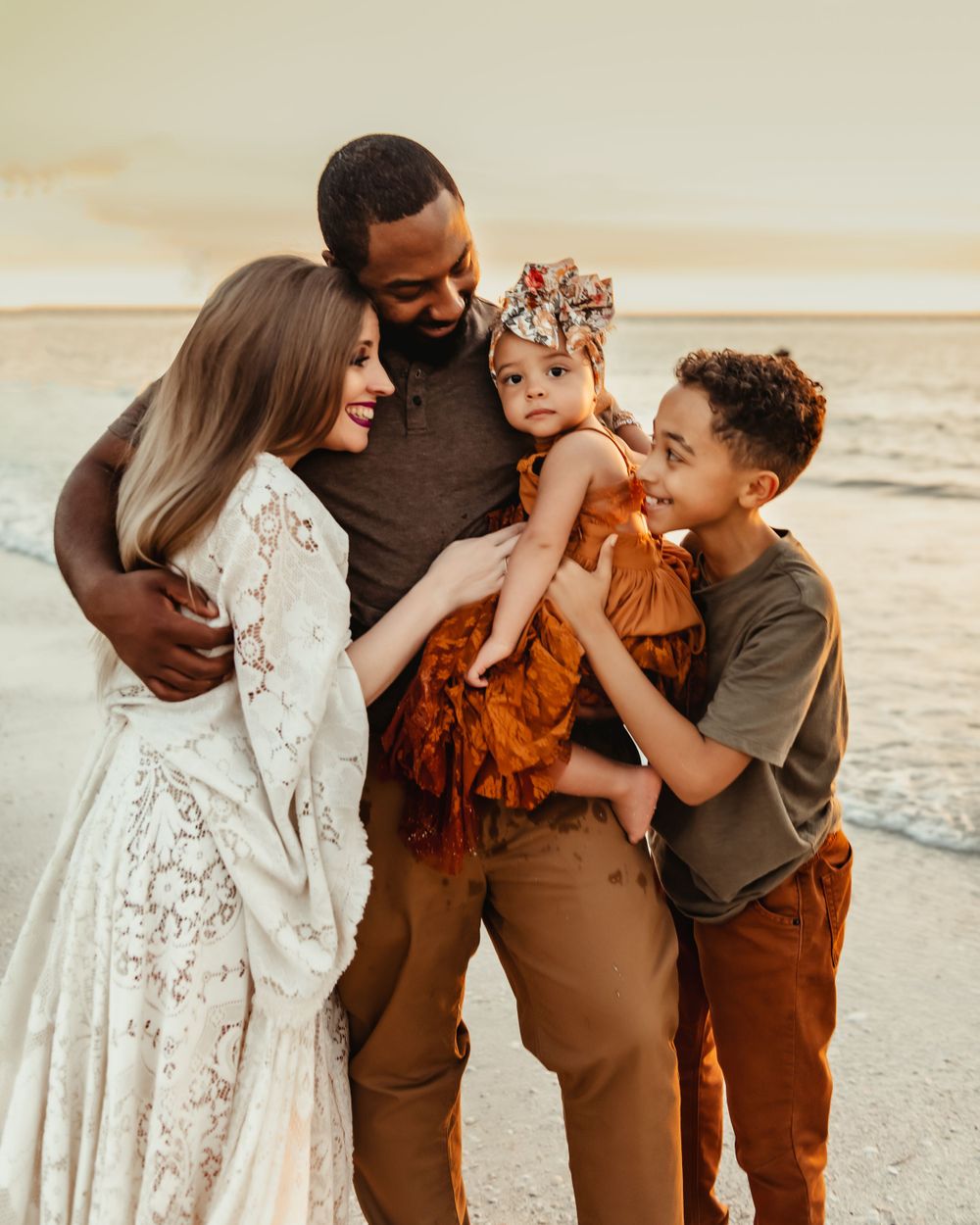 Happy interracial family of four smiling together on a sandy beach.
