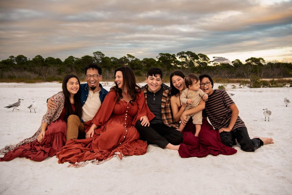 Family group sitting together on white sand beach at sunset.