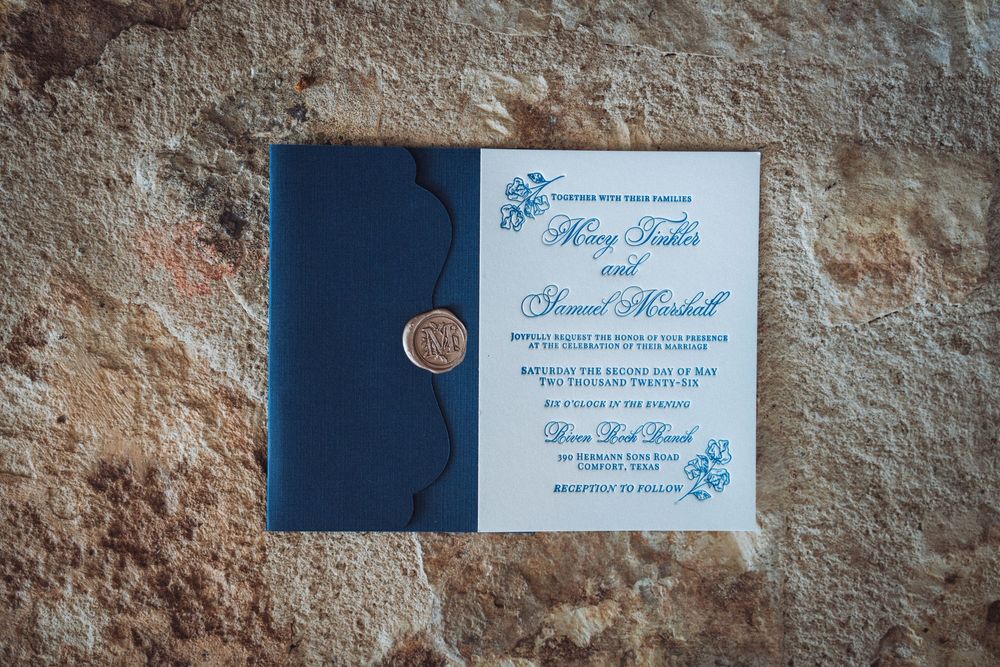 Elegant navy blue wedding invitation suite with wax seal, featuring blue floral details on textured stone background.