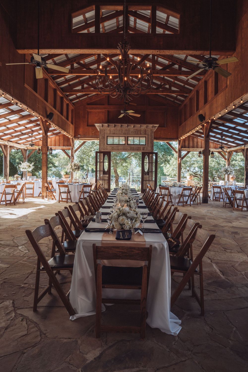 Elegant rustic barn wedding reception with long wooden tables, white linens, and chandelier lighting.