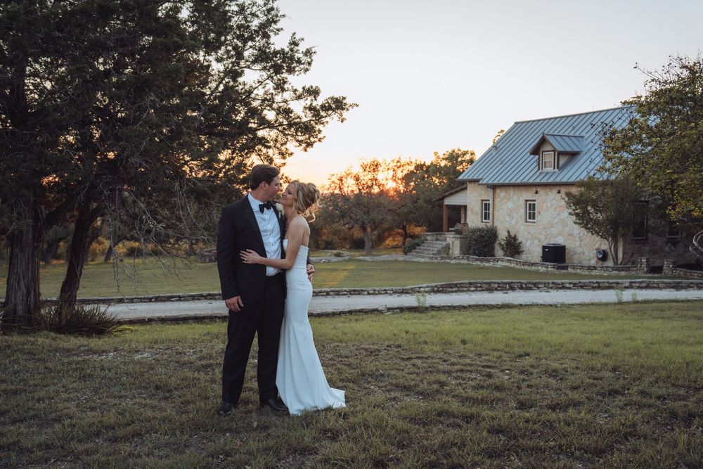 Bride and groom share a romantic moment at golden hour outside a rustic stone wedding venue.