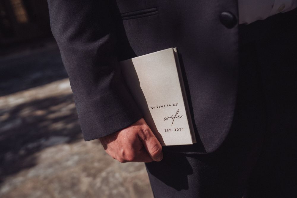 Groom in dark suit holding a letter to his wife on wedding day.