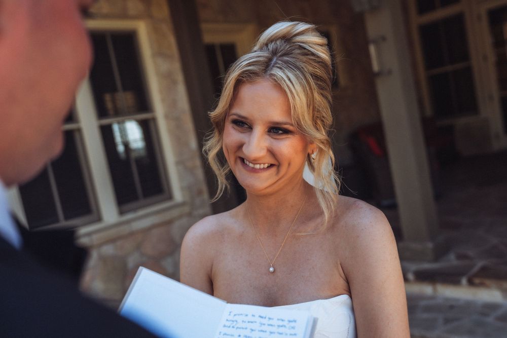 Bride smiling while reading wedding vows outdoors on her special day.