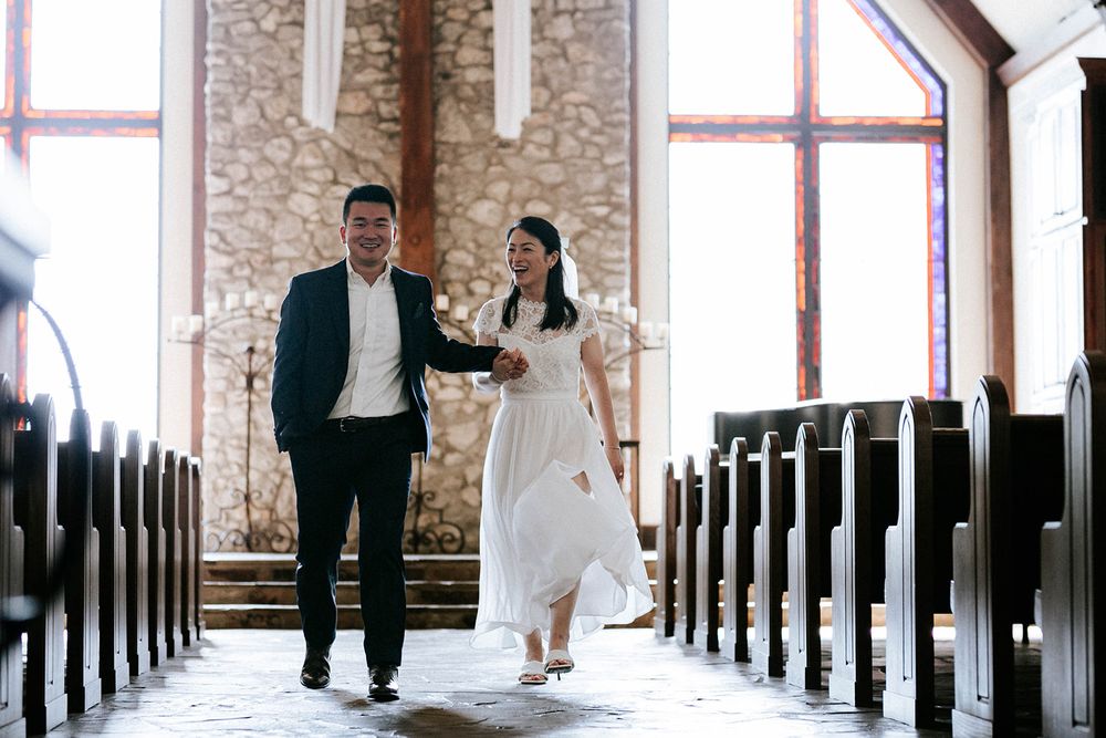 Newlyweds walking hand in hand down the aisle of a stone chapel at their Fayetteville, Arkansas elopement