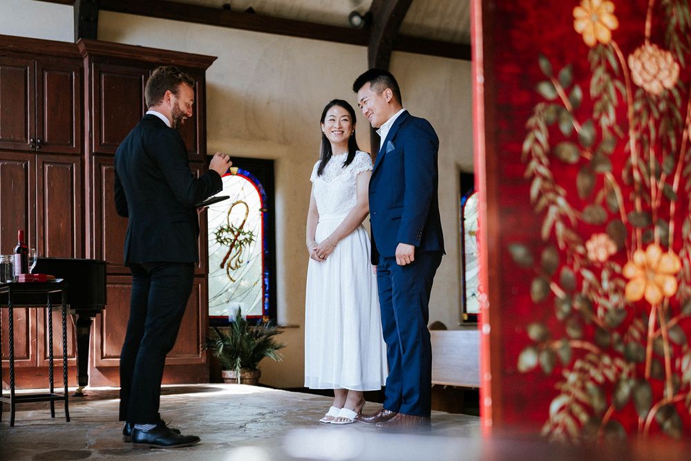 Couple exchanging vows with their officiant beside an ornate floral panel at their Fayetteville, Arkansas chapel wedding