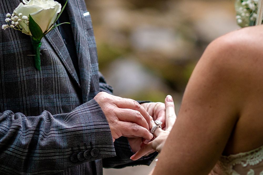 Close-up of the groom's white rose boutonniere as he holds the bride's hand at their Mirror Lake elopement, Mountain View, Arkansas