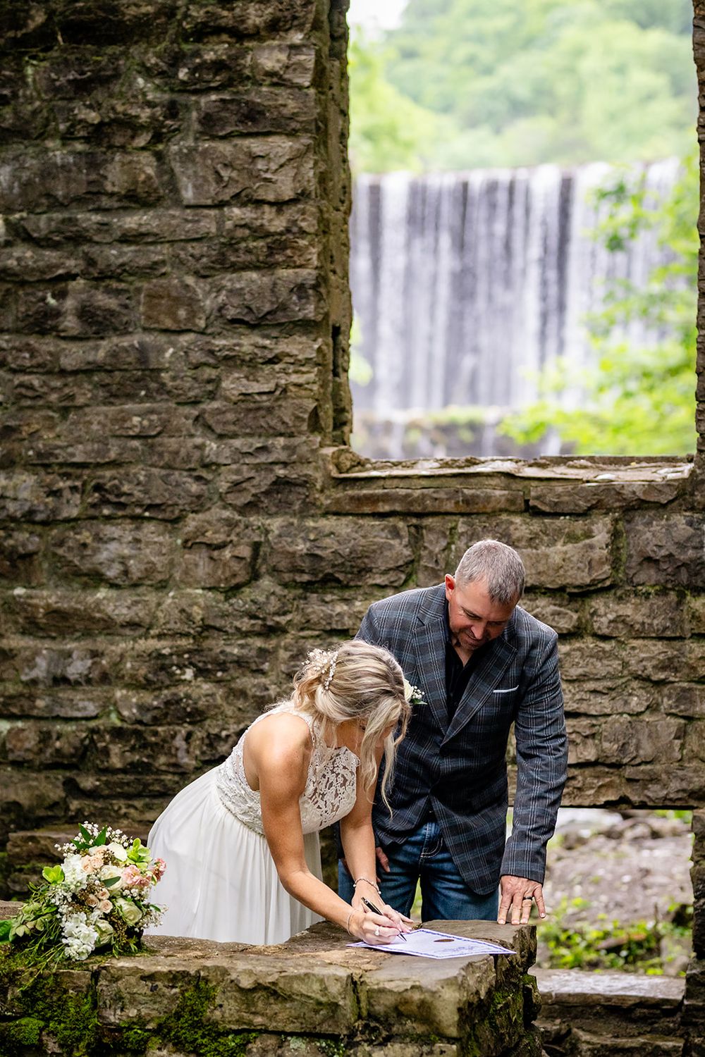 Bride signing the marriage license on a stone ledge overlooking Mirror Lake Waterfall, Mountain View, Arkansas