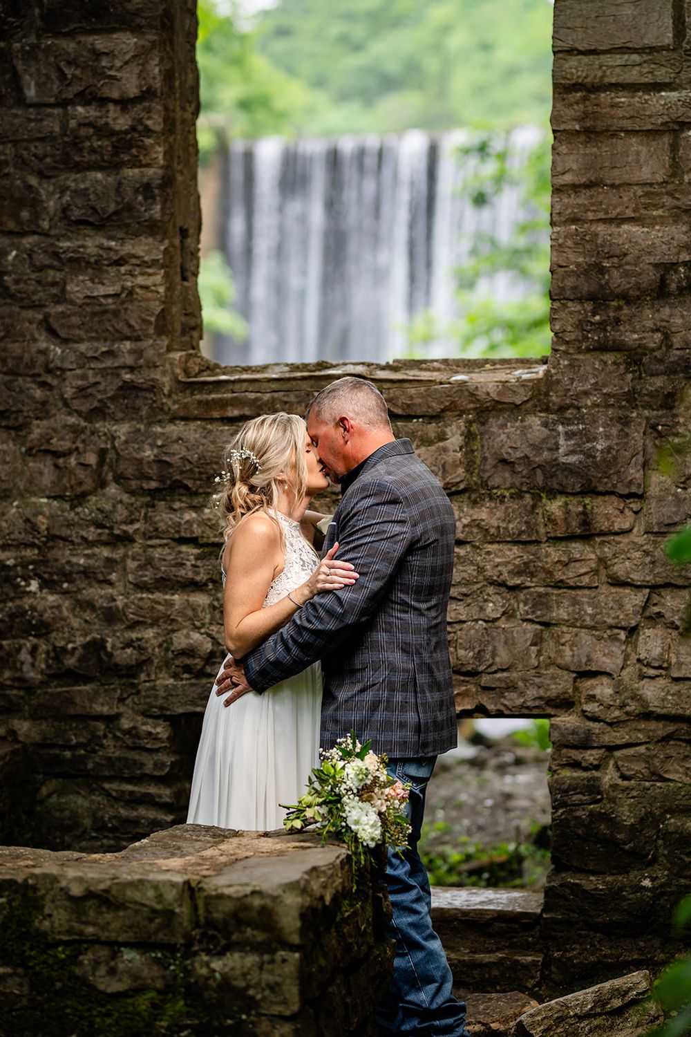 Bride and groom in the historic stone mill ruins with Mirror Lake Waterfall framed behind them, Mountain View, Arkansas