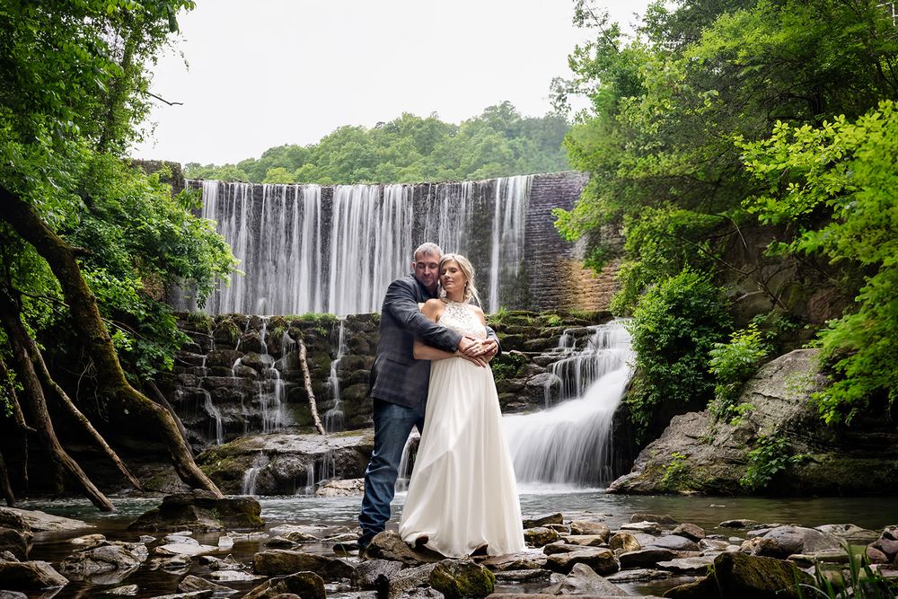 Bride and groom embracing in front of Mirror Lake Waterfall in Mountain View, Arkansas
