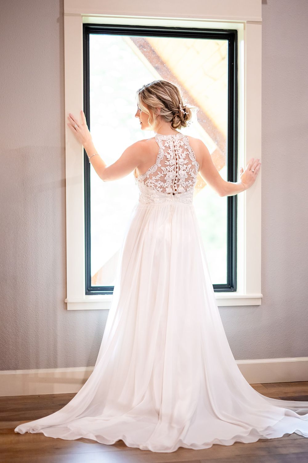 Bride in a lace-back wedding gown backlit at a window before her Mirror Lake elopement in Mountain View, Arkansas