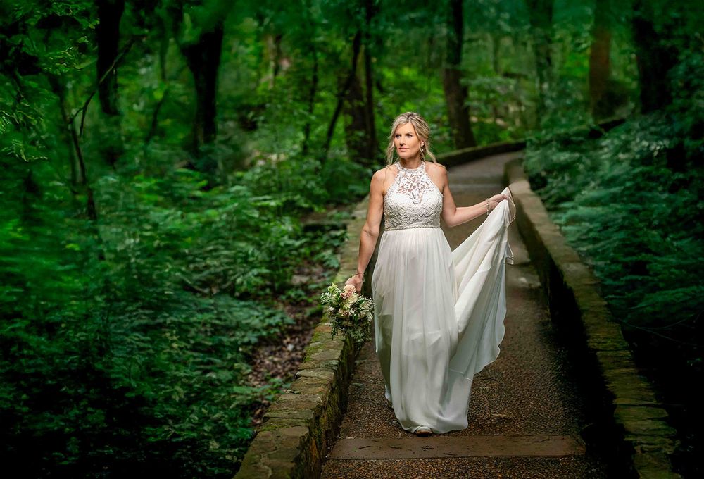 Bride holding her gown on a mossy stone path through the Ozark woods at Mirror Lake, Mountain View, Arkansas