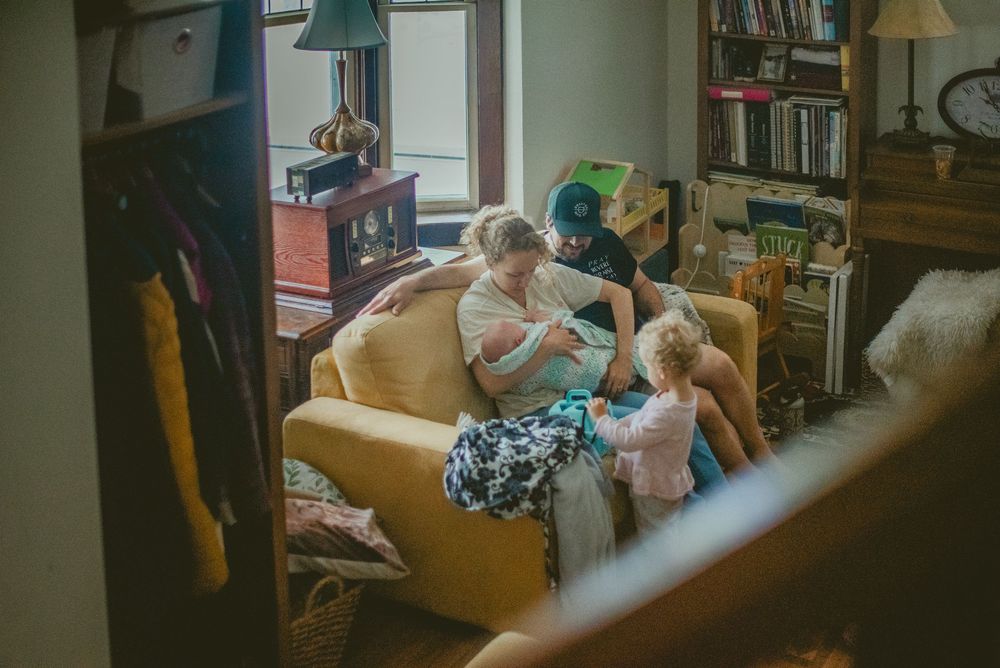 Family gathered on a yellow sofa in a cozy living room with bookshelves, sharing a warm moment together. documentary in home photography