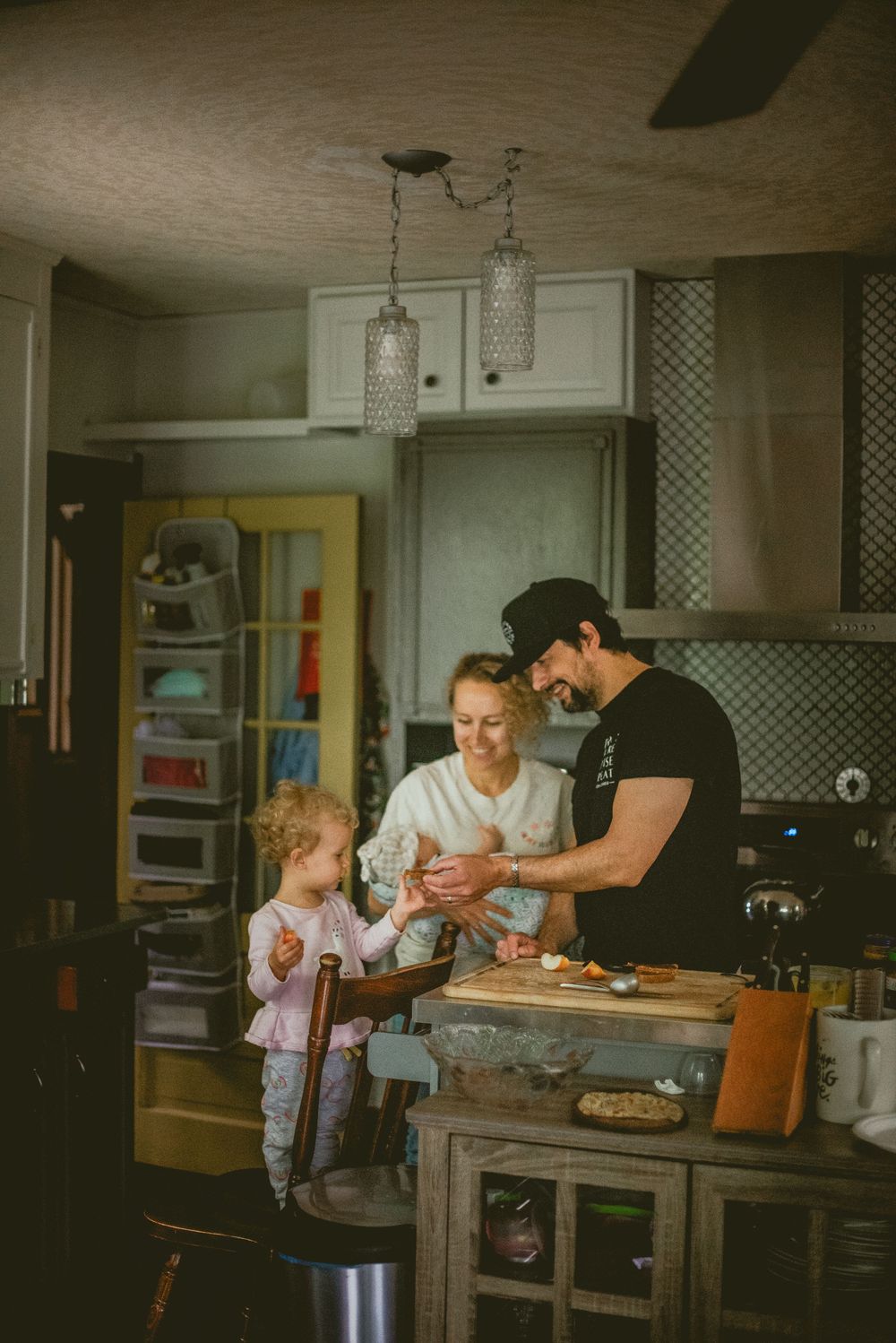 Family of three sharing a joyful cooking moment together in a cozy, warmly lit kitchen. documentary in home photography