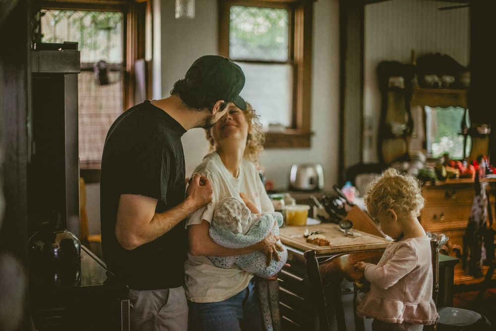 Family sharing a tender moment in a rustic kitchen, with a man, woman, and young child cooking together. documentary in home photography