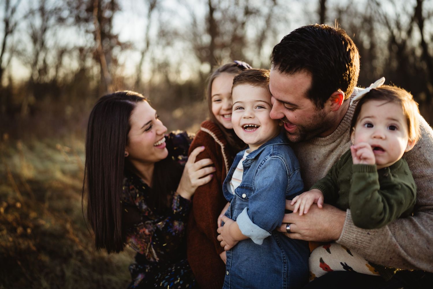 Family sharing joyful laughter together during golden hour outdoor photoshoot in nature.