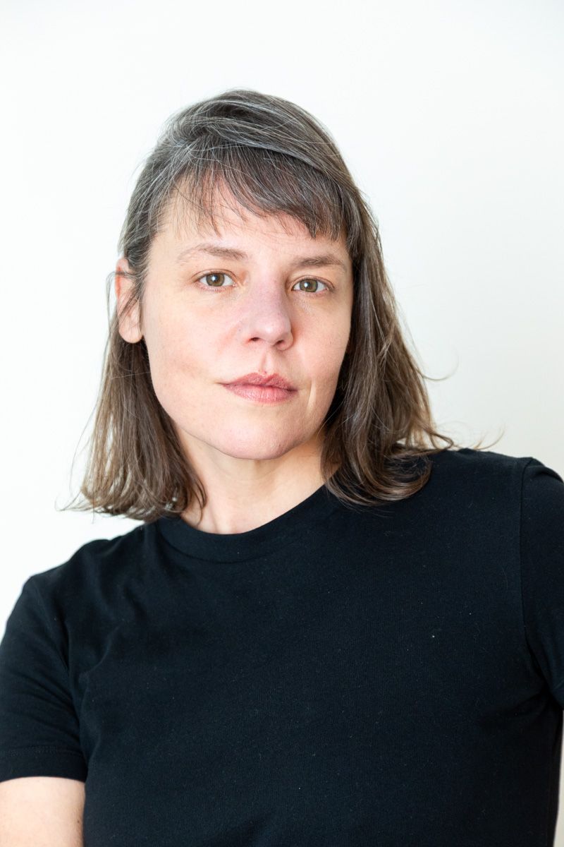 Middle-aged woman with shoulder-length brown hair wearing a black t-shirt poses against a white background.