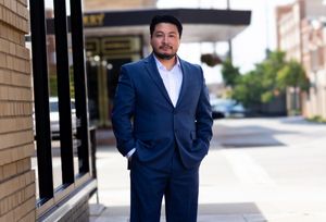 Professional man in navy blue suit standing on urban sidewalk outside a building on a sunny day.