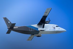 A small commuter aircraft with blue and white livery flies against a vivid blue sky.