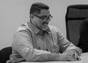 Black and white portrait of a smiling man with glasses seated at a table.