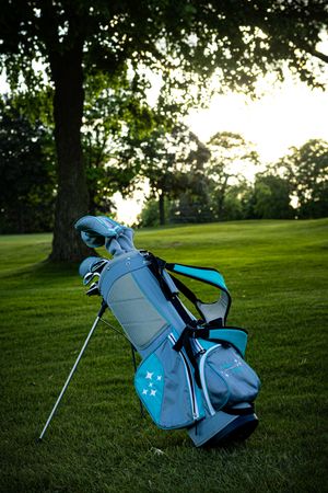 Light blue and gray golf stand bag on green fairway at sunset.