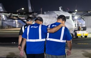 Two ground crew members in blue safety vests stand beside a cargo aircraft at night.