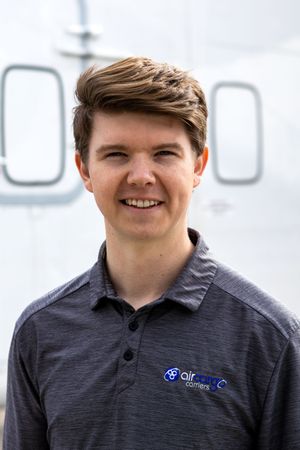Young man smiling in Air Cargo Carriers polo shirt in front of aircraft.
