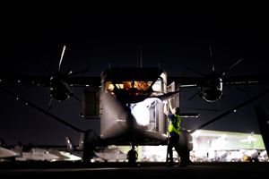 Ground crew performs nighttime pre-flight checks on a twin-engine cargo aircraft on the tarmac.