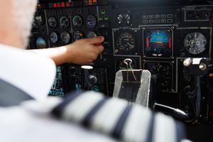 A uniformed pilot adjusts controls on a complex aircraft instrument panel in the cockpit.