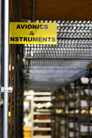 Yellow shelf label reading Avionics and Instruments in an aircraft parts storage warehouse.
