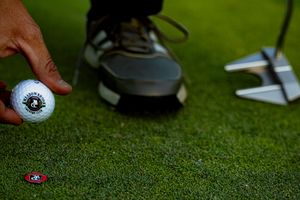 Golfer placing a branded golf ball on a green putting surface near a hole marker.