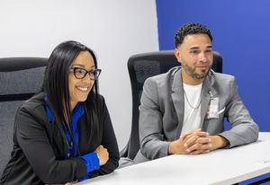 Two smiling professionals sitting at a conference table in a modern office setting.