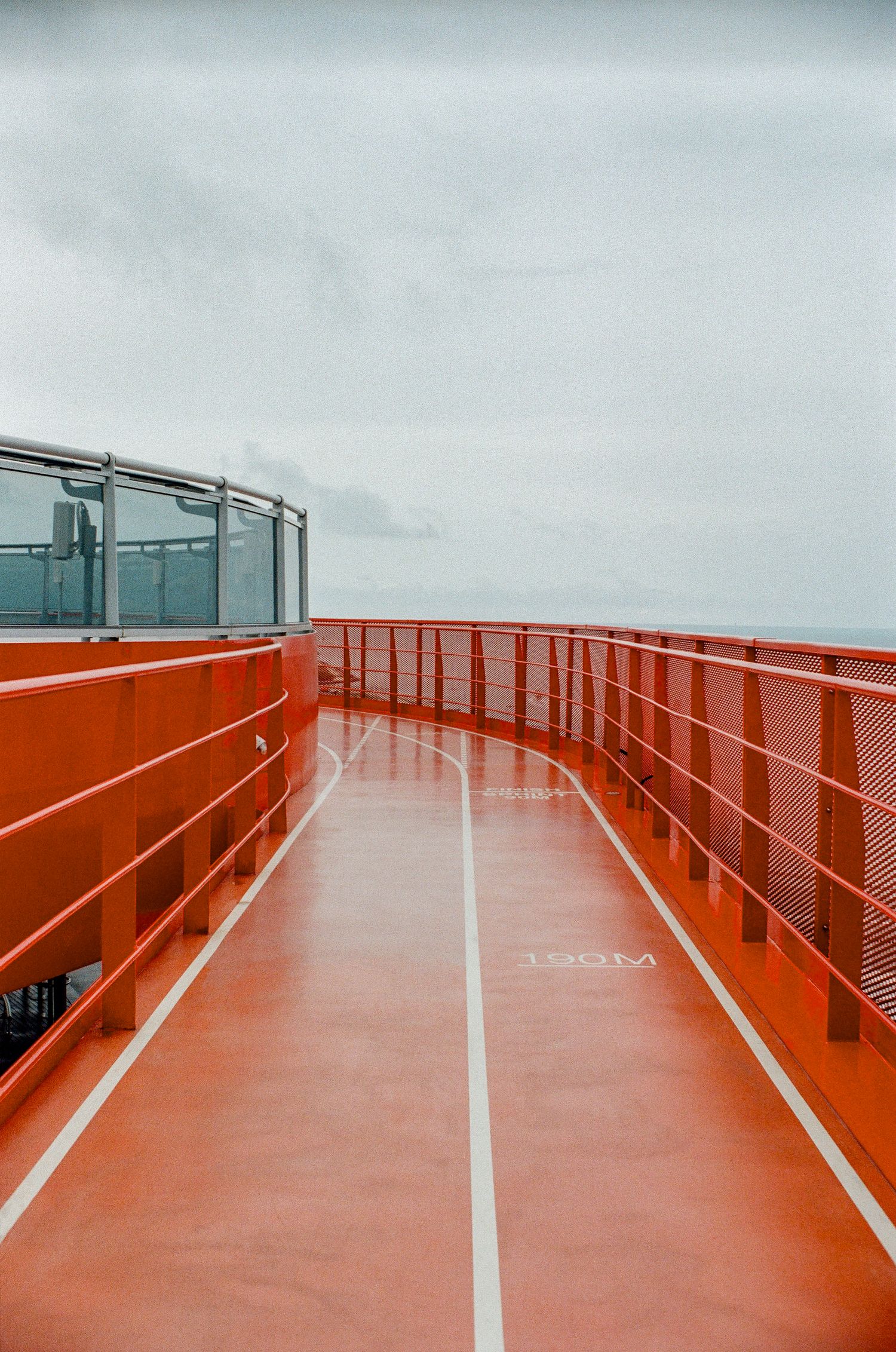 Red walkway with orange railings on a ferry deck under an overcast sky, leading to the horizon.