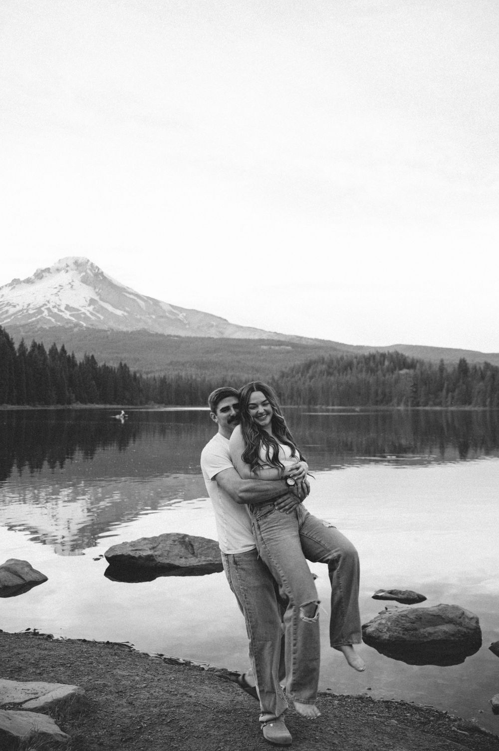 Couple embracing and smiling by Trillium Lake with Mount Hood reflected in the water, black and white photo.
