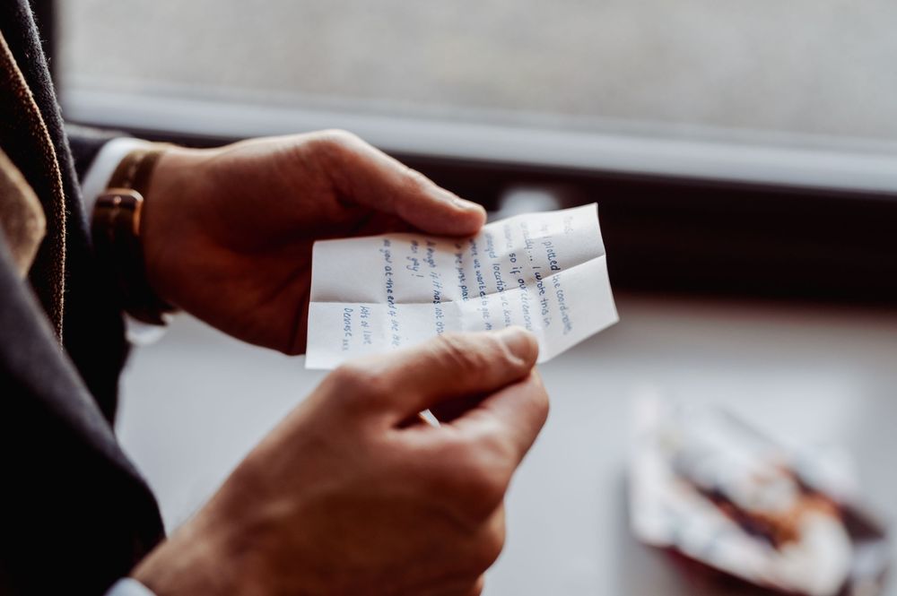 Person holding a small handwritten note near a window with blurred background.
